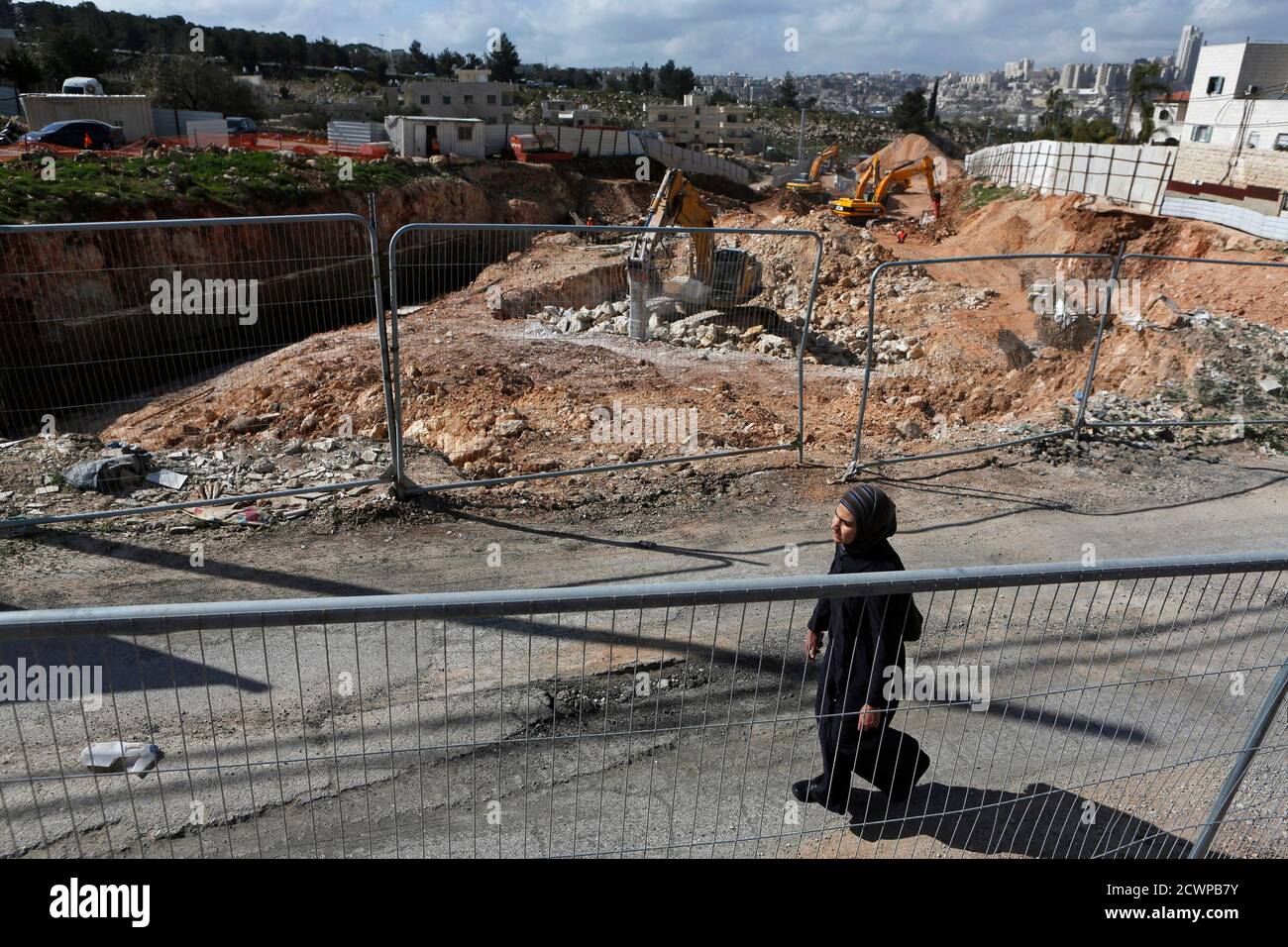 A woman walks past a road under construction in the Arab neighbourhood of Beit Safafa in Jerusalem February 28, 2013. The mechanical diggers start work soon after dawn, cutting through a leafy village on the outskirts of Jerusalem to build a six-lane highway that has become the latest focal point of Arab-Israeli discontent. The road leads directly to Jewish settlements, built on occupied land around the foothills of Bethlehem. When finished, it will allow the settlers to speed down to Israel's thriving coastal plains, unhindered by traffic lights or roundabouts.  Their gain is coming at the ex Stock Photo