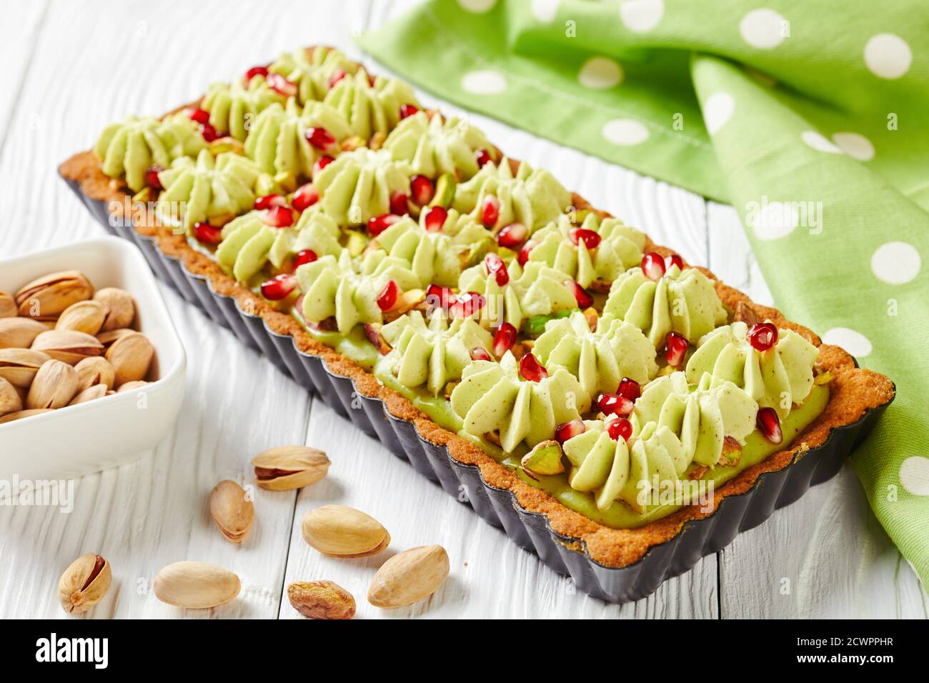 Pistachio ganache tart with pomegranate seeds on a square baking tin