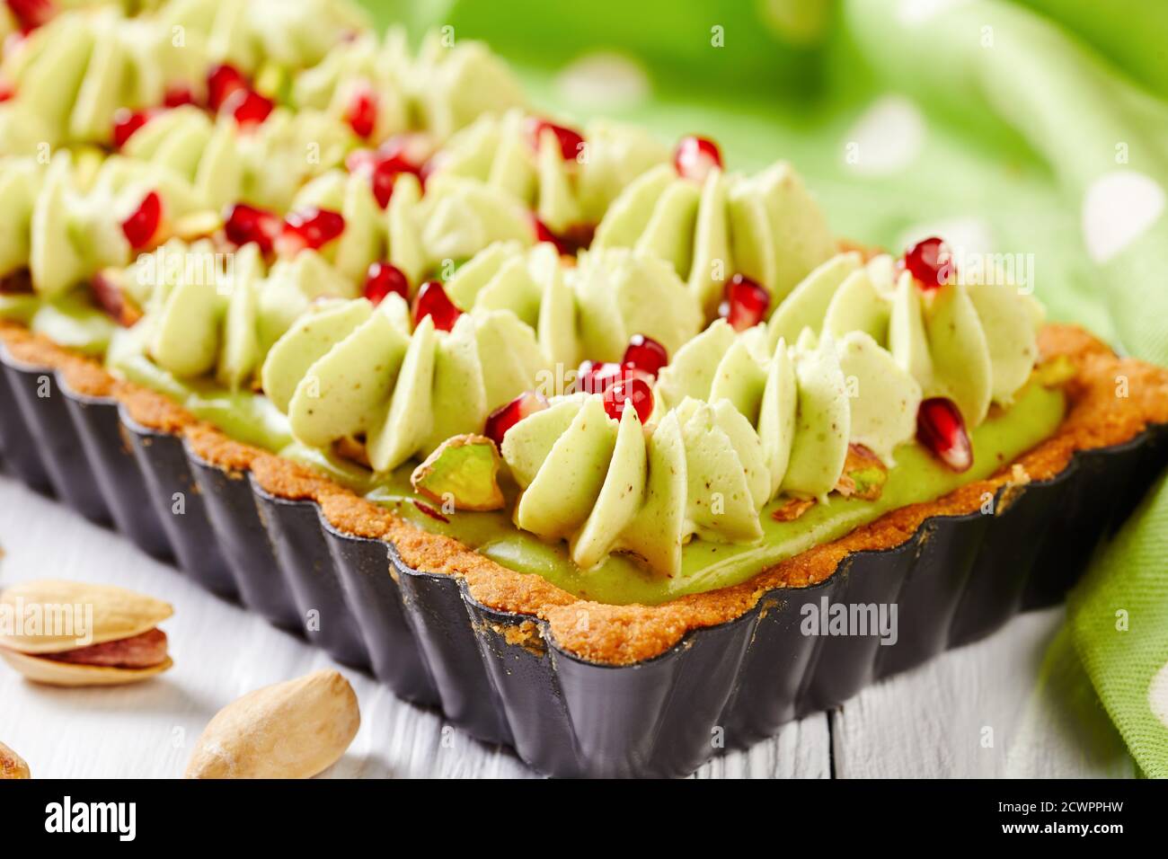 Pistachio ganache tart with pomegranate seeds on a square baking tin