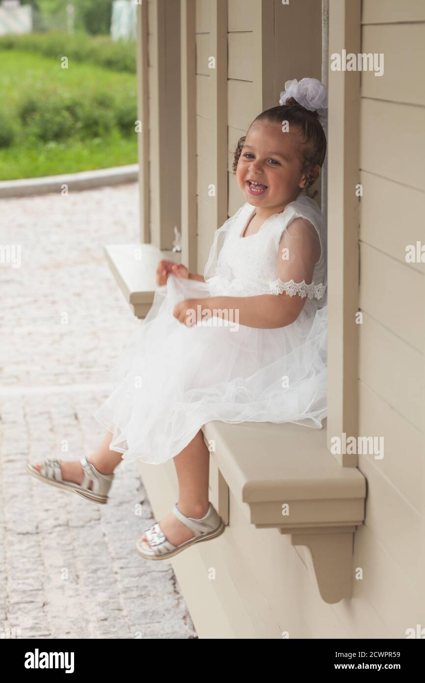 A little girl in a white dress of the bride sits on a windowsill Stock ...