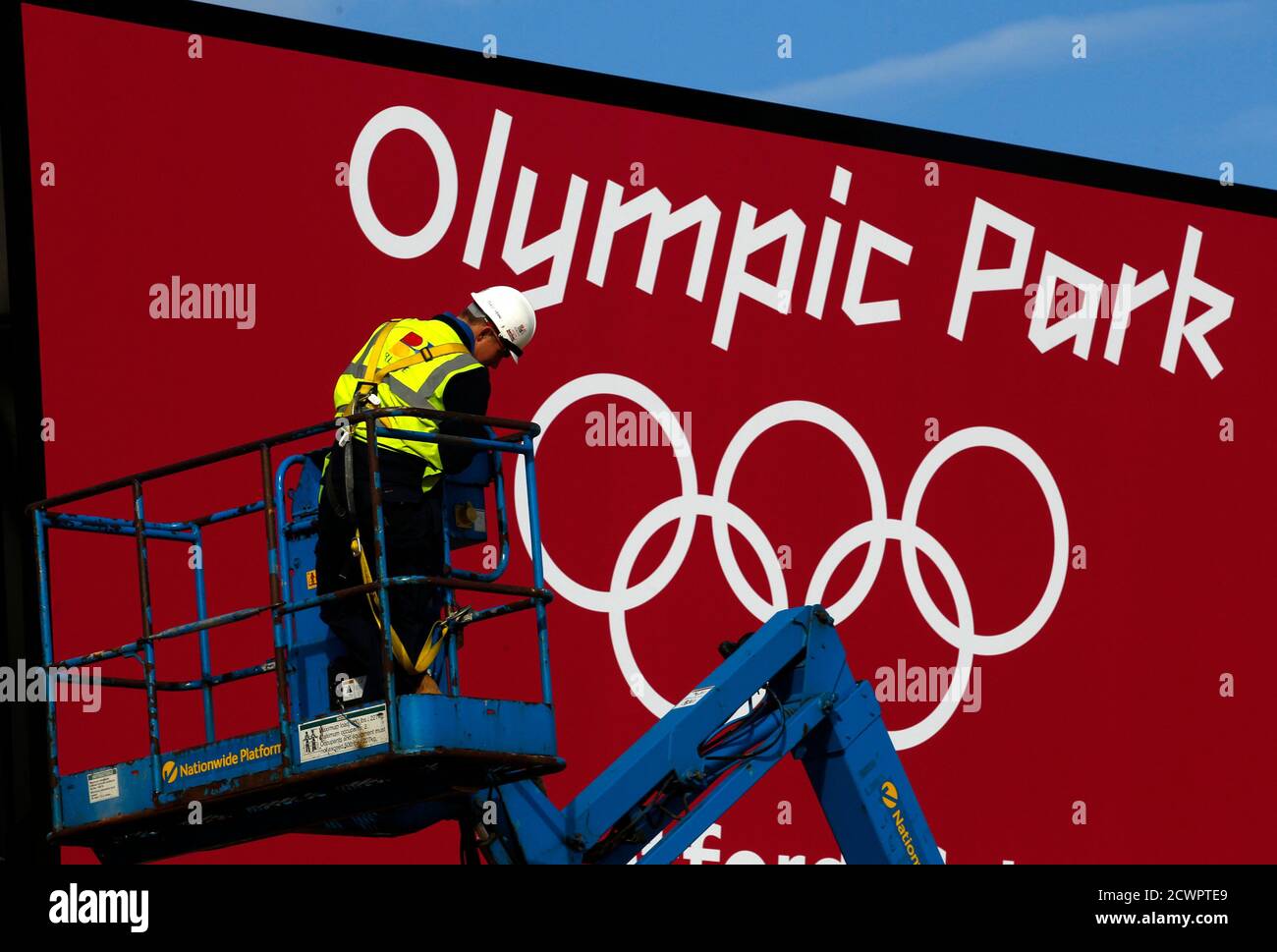 A worker adjusts his position on a cherry picker in front of one of the signs at the entrance to the Olympic Park, Stratford, east London, July 19, 2012. The 2012 London Olympic Games will begin in just over a week.  REUTERS/Andrew Winning (BRITAIN) Stock Photo