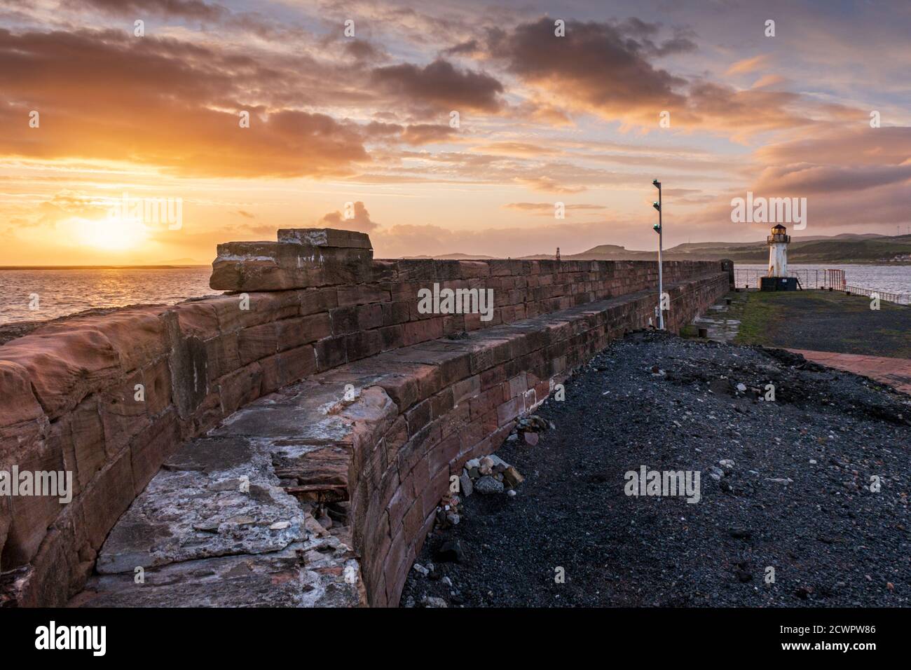 Ardrossan harbour wall and lighthouse guarding the harbor entrance to Ardrossan port on the Firth of Clyde at sunset, North Ayrshire, Scotland. Stock Photo