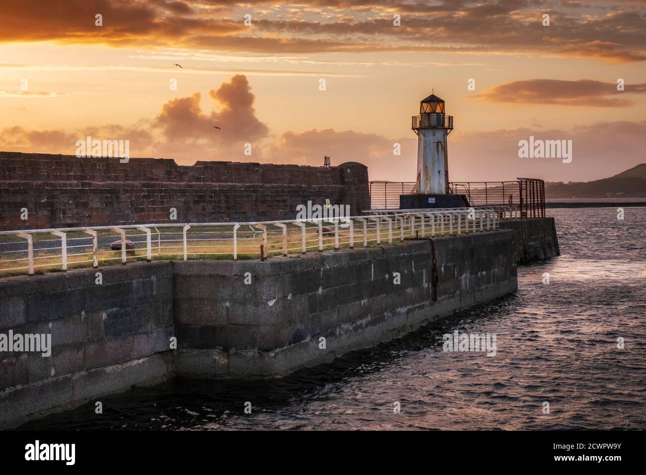 Ardrossan harbour wall and lighthouse guarding the harbor entrance to Ardrossan port on the Firth of Clyde at sunset, North Ayrshire, Scotland. Stock Photo