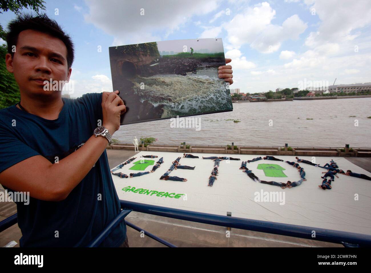 A Greenpeace activist shows a picture of what he claims to be waste waters  being released into river in China as others form a human banner with  message "Detox" at Santichaiprakarn Park,
