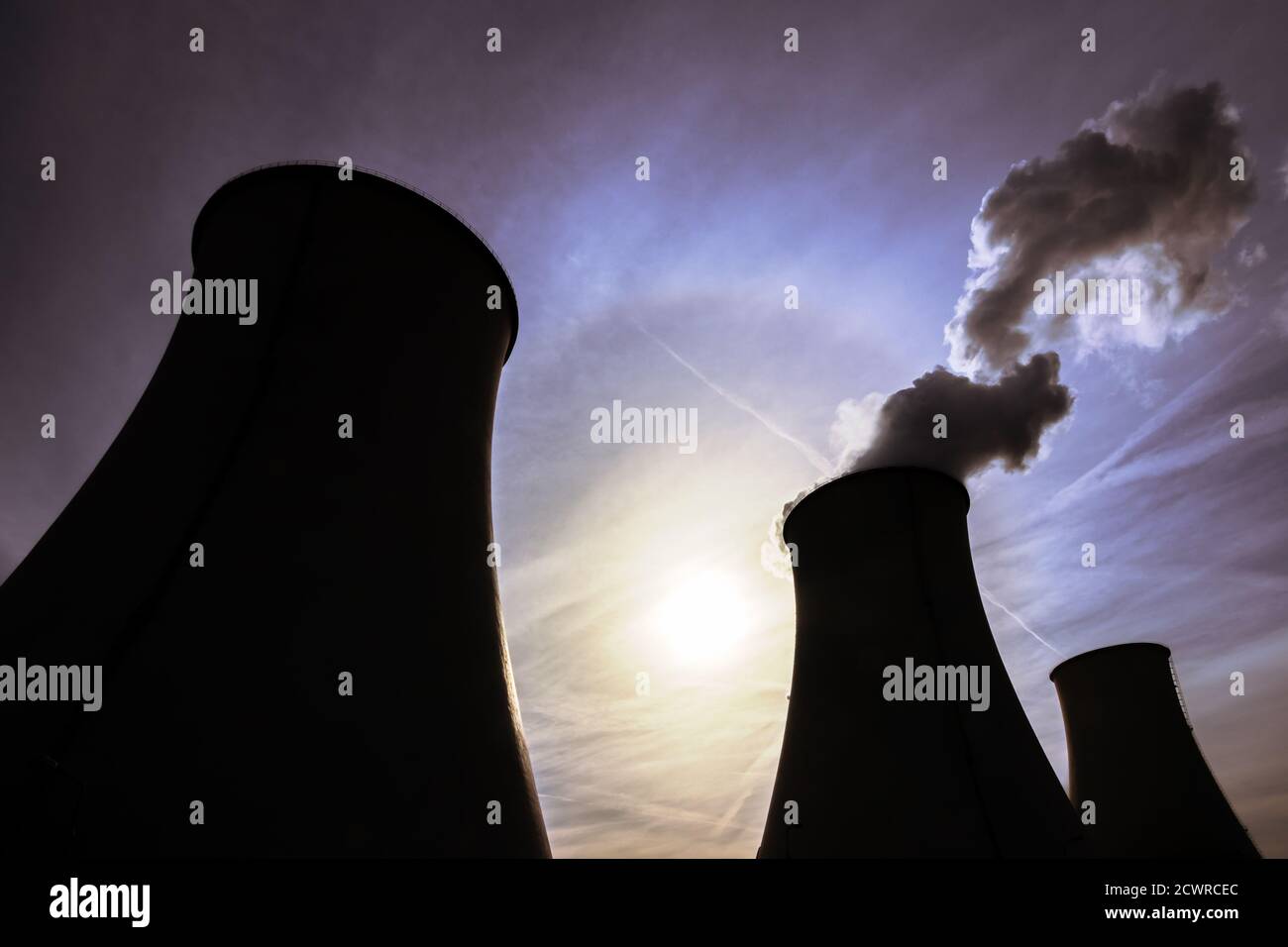 Silhouettes of cooling towers with the sun in the background Stock Photo