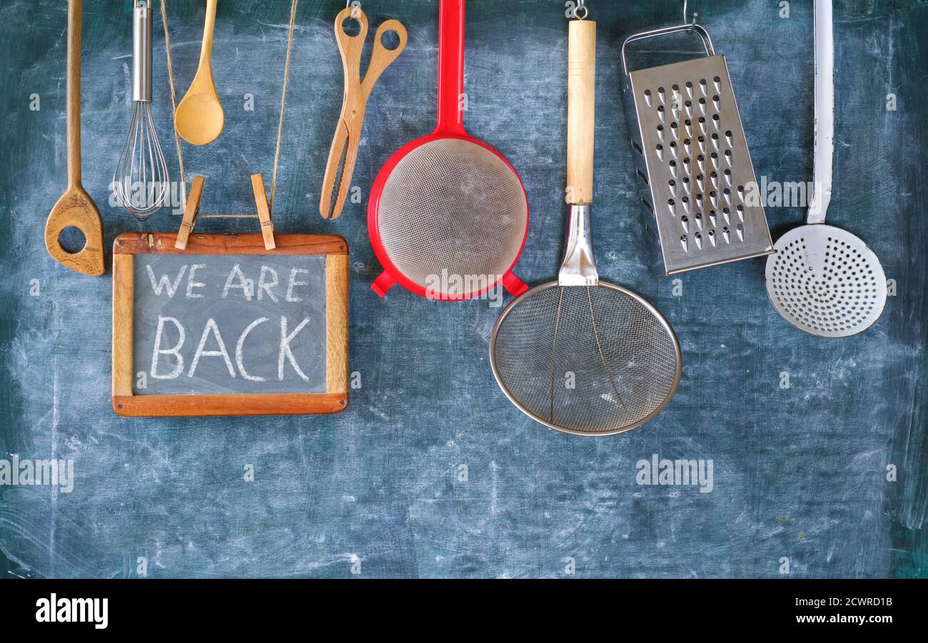 Restaurant announcing reopening after corona virus lockdown, kitchen utensils and message we are back on black board,back to gastronomy business Stock Photo