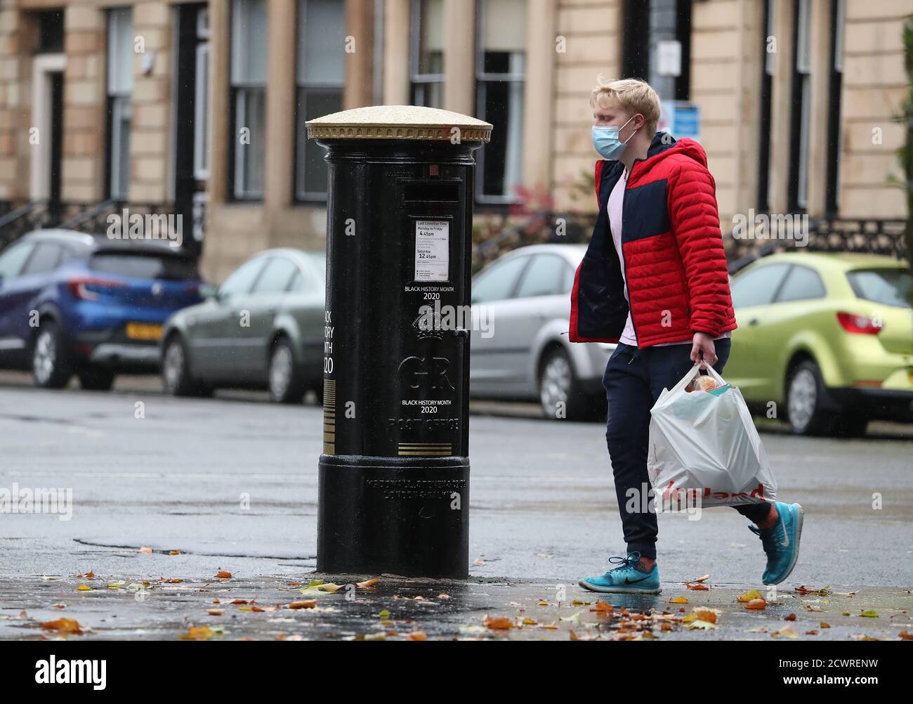 A member of the public walks past a black postbox featuring an image of Second Lieutenant Walter Tull, on Byres Road, Glasgow, one of four special edition postboxes unveiled by Royal Mail to mark Black History Month. Stock Photo