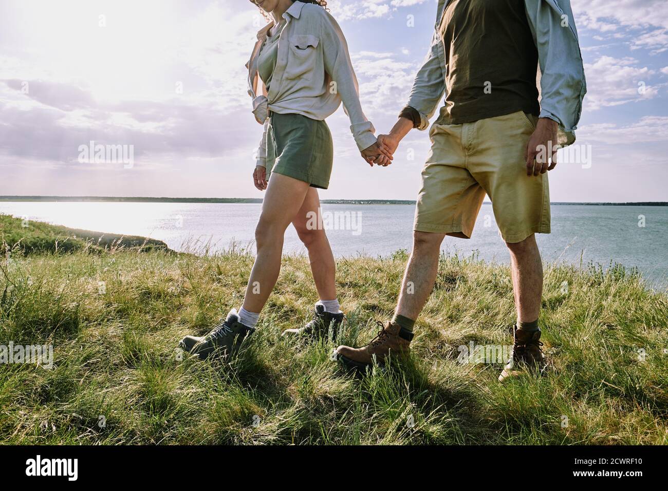 Unrecognizable couple of hikers holding hands and walking on grass together while enjoying travel Stock Photo