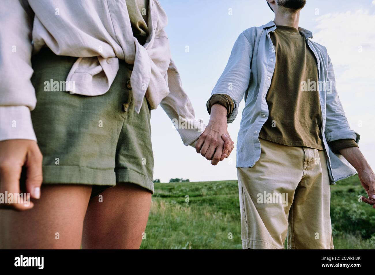 Close-up of unrecognizable travelling couple in casual shirts holding hands in hills while standing in field Stock Photo