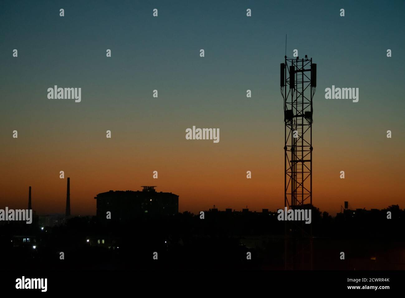 Night landscape, silhouette of city buildings and communication tower mobile operator antenna against the background of sunset and blue sky Stock Photo