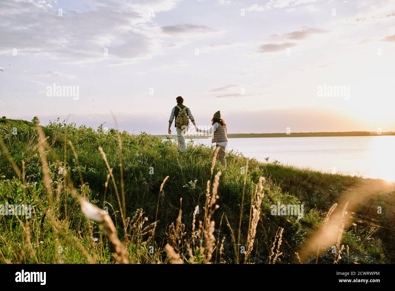 Rear view of young man holding hand of girlfriend while they hiking hills together at sunset Stock Photo