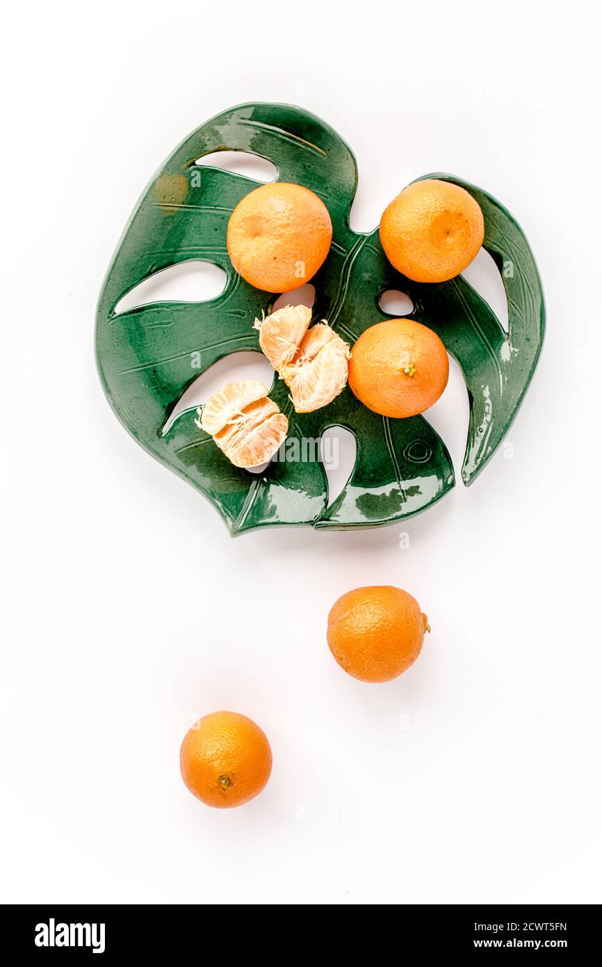 Ceramic plate-leaf Monstera with tangerines isolated on white background. Flat lay, top view.  Stock Photo