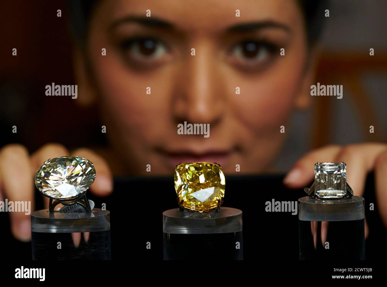 A model poses behind a 103.46 carats diamond ring (L) a vivid yellow 100.09  carats diamond (C) and The Victory diamond (31.34 carats) during an auction  preview at Sotheby's in Geneva May