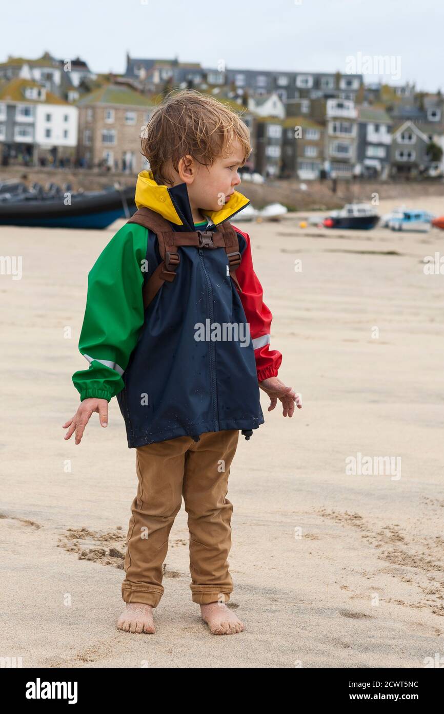 Little boy (2/3 years old), wearing a colourful coat, playing on the sand on a chilly, overcast morning: St. Ives harbour, Cornwall, UK. MODEL RELEASED Stock Photo
