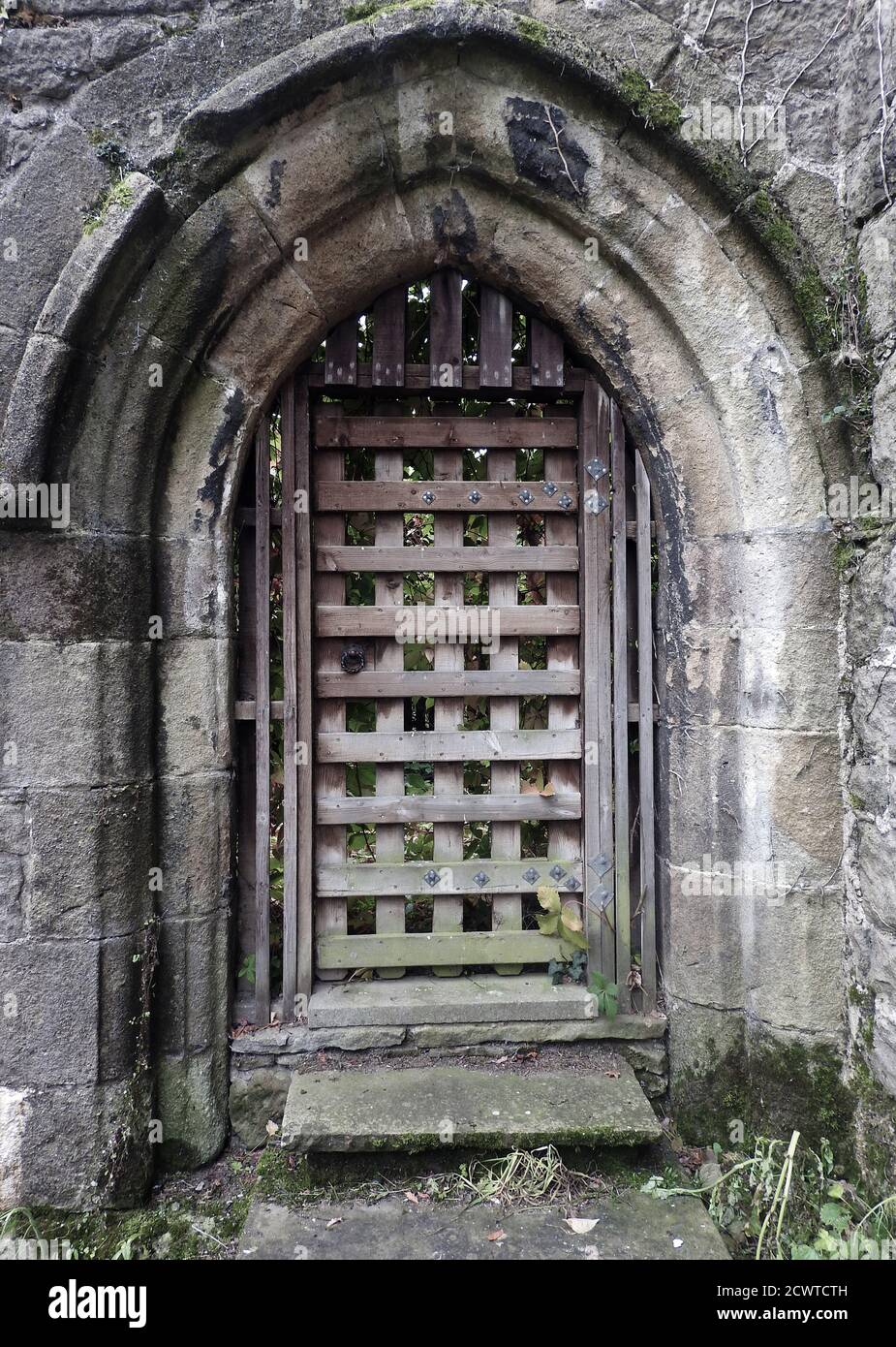 A Romanesque gothic style stone arched doorway at Whalley Abbey,  Lancashire, UK.  with  latticed  inner grille door made of wood. Though most of the buildings were demolished,  a number of walls and features remain and foundations of other parts have been excavated  and left on view. The  abbey closed in 1537  during the dissolution of the monasteries in the same year that  Abbot  John Paslew was executed for high treason for his part in   the Pilgrimage of Grace events of the previous year Stock Photo