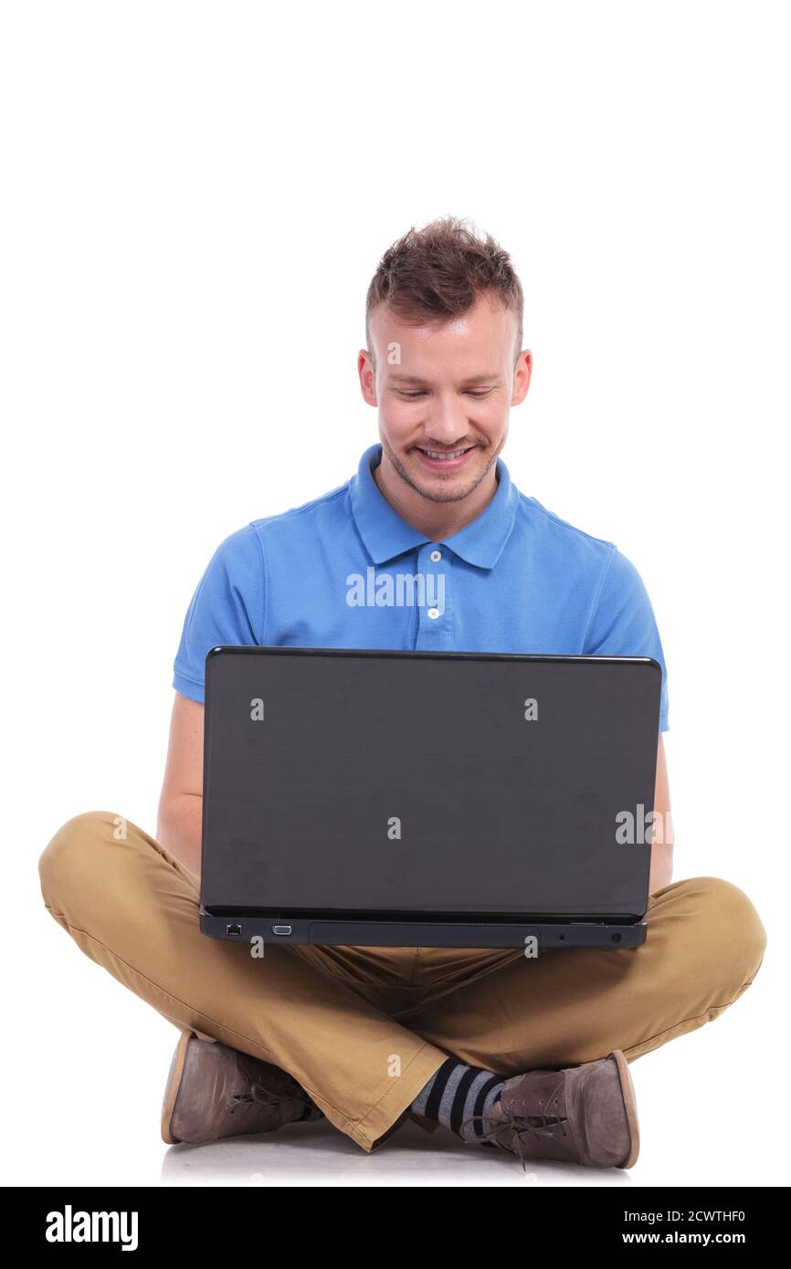 casual young man sitting on the floor with his legs crossed and working ...