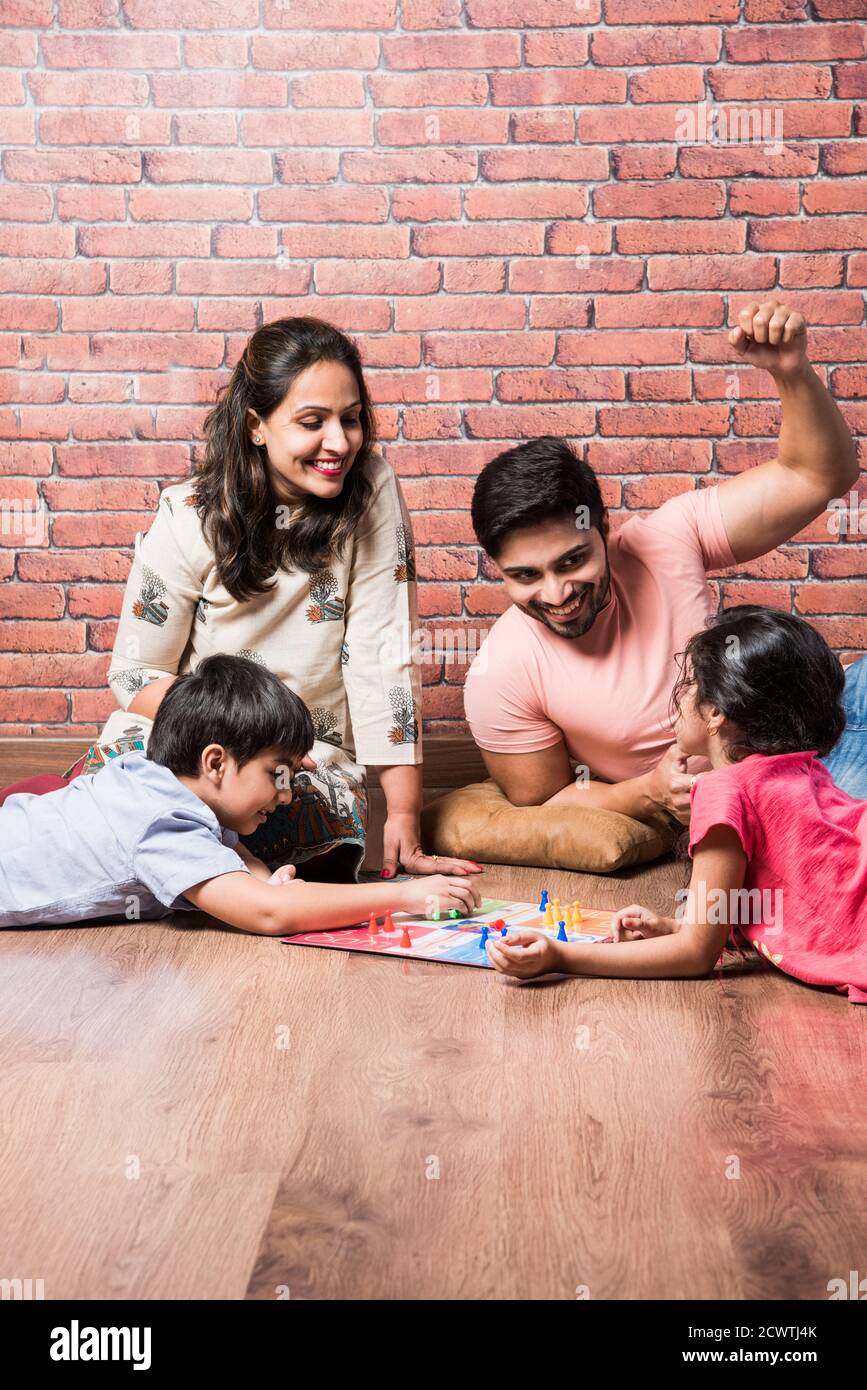 Indian young family of four playing board games like Chess, Ludo or Snack and Ladder at home in quarantine Stock Photo