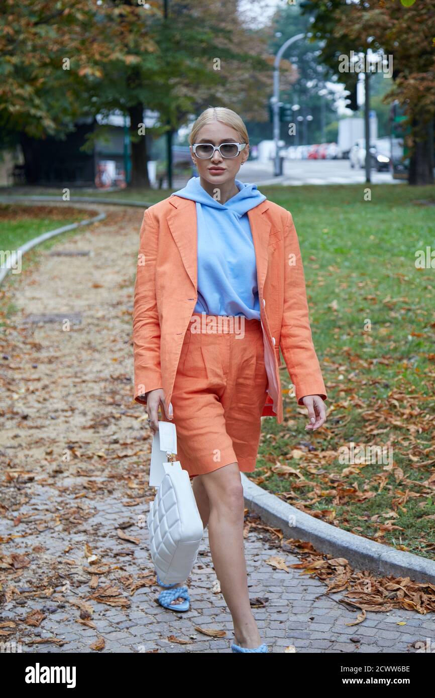 MILAN, ITALY - SEPTEMBER 25, 2020: Woman with orange jacket and pale blue hoodie walking before Sportmax fashion show, Milan Fashion Week street style Stock Photo