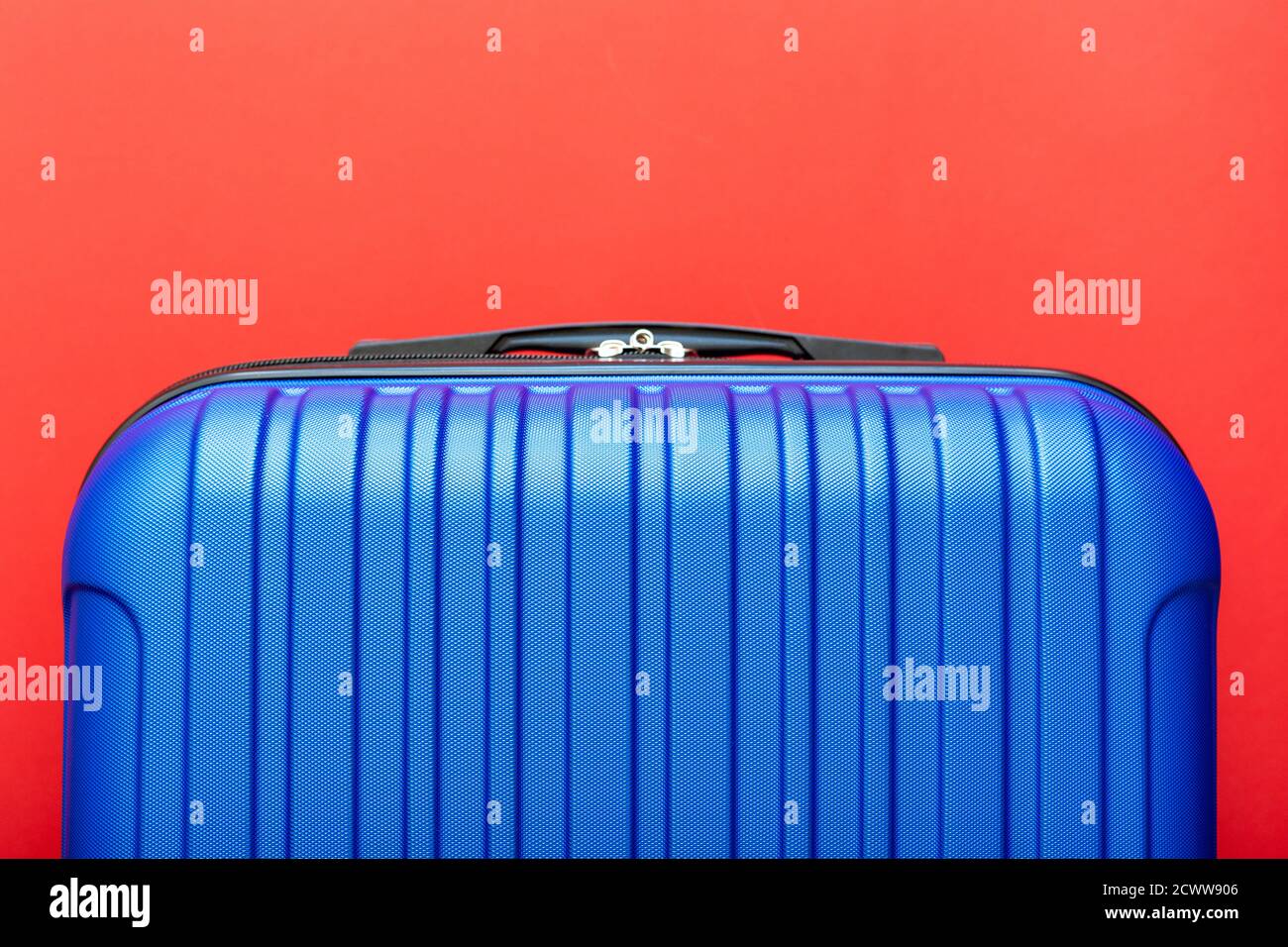 Modern blue suitcase on red background close up with copy space for text. Minimal style travel concept. Vacation trip. Summer holiday stock photo Stock Photo