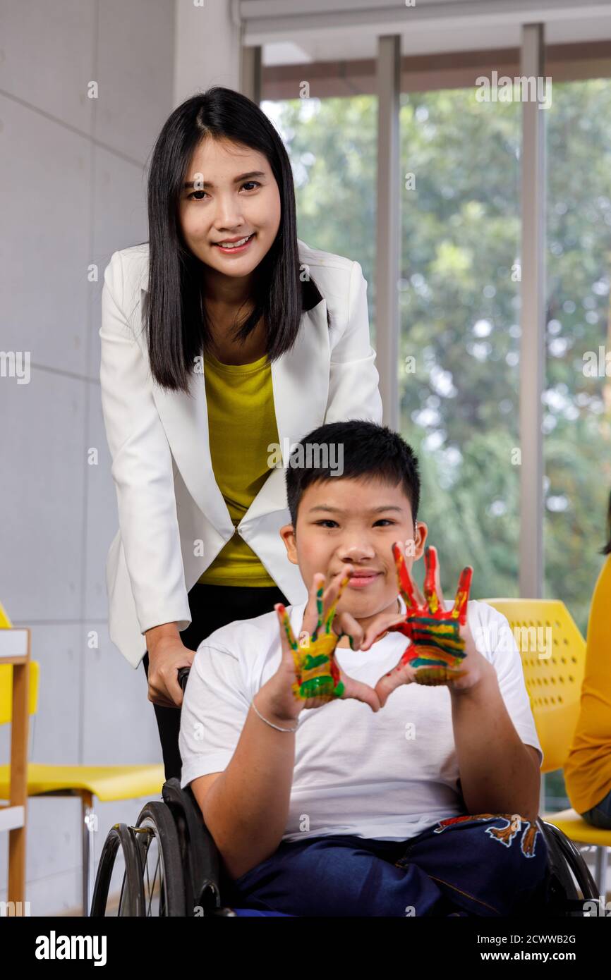 Disabled boy in wheelchair painted with his teacher. Concept children learning in school. Stock Photo