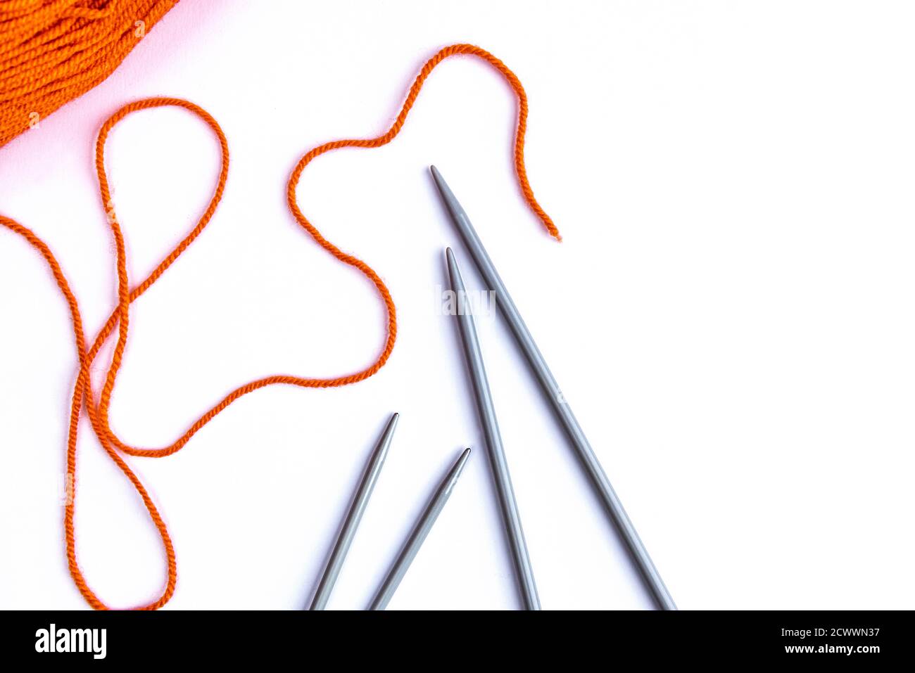 Knitting needles and orange wool on white background. Stock Photo