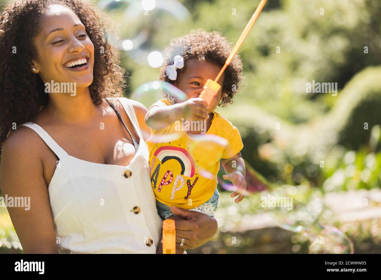 Happy mother and toddler daughter playing with bubble wand in sunshine Stock Photo