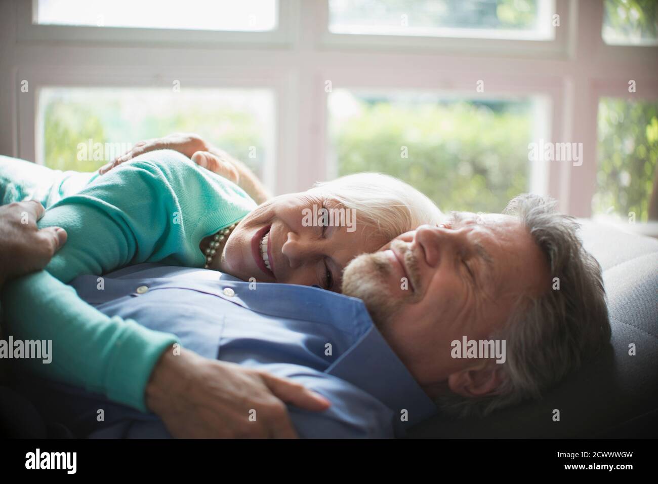 Happy senior couple cuddling by sunny window Stock Photo