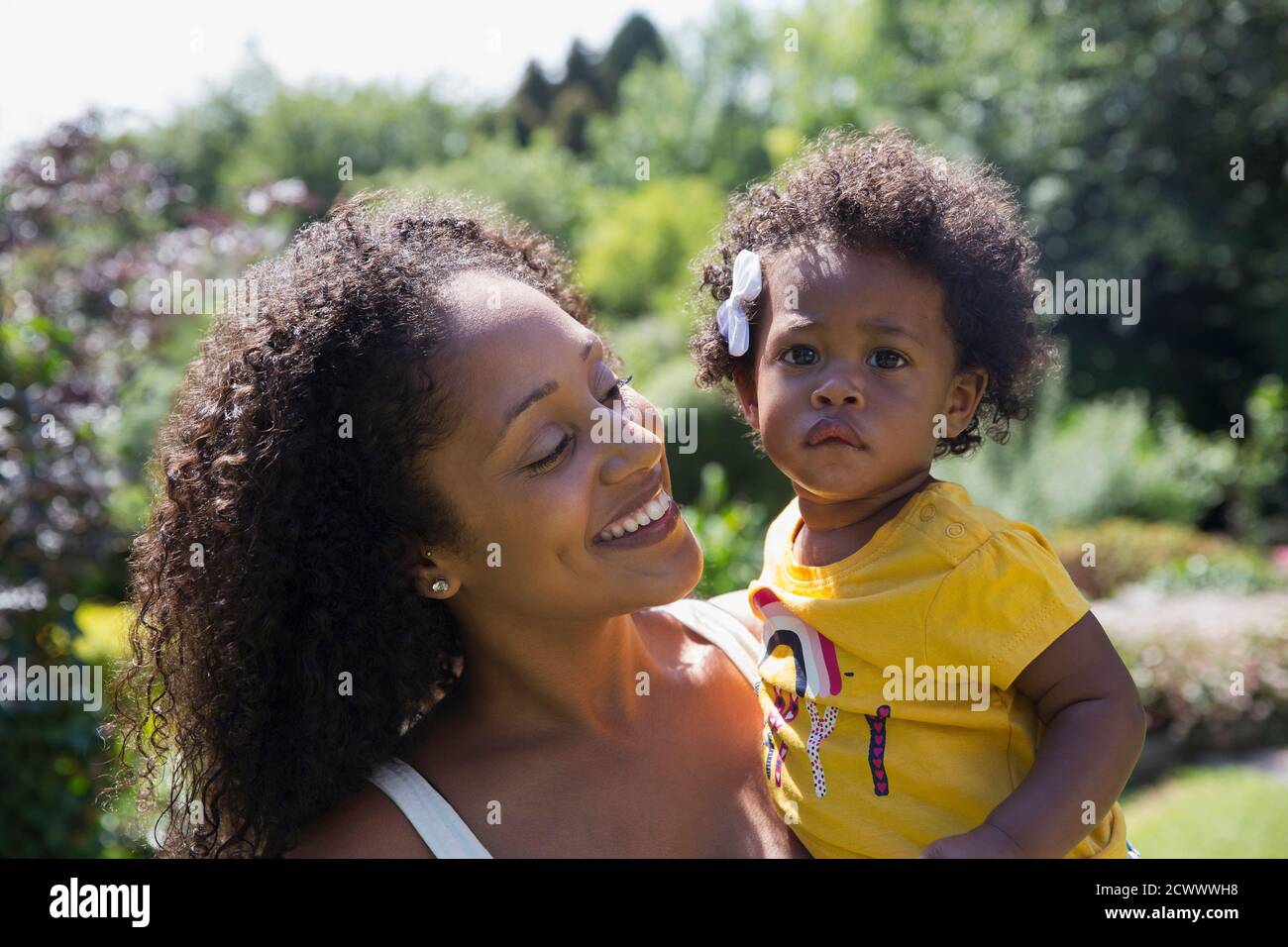 Portrait happy mother holding cute toddler daughter in sunny yard Stock Photo