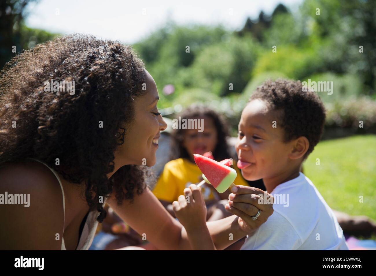 Playful mother and son eating watermelon popsicles on sunny patio Stock Photo