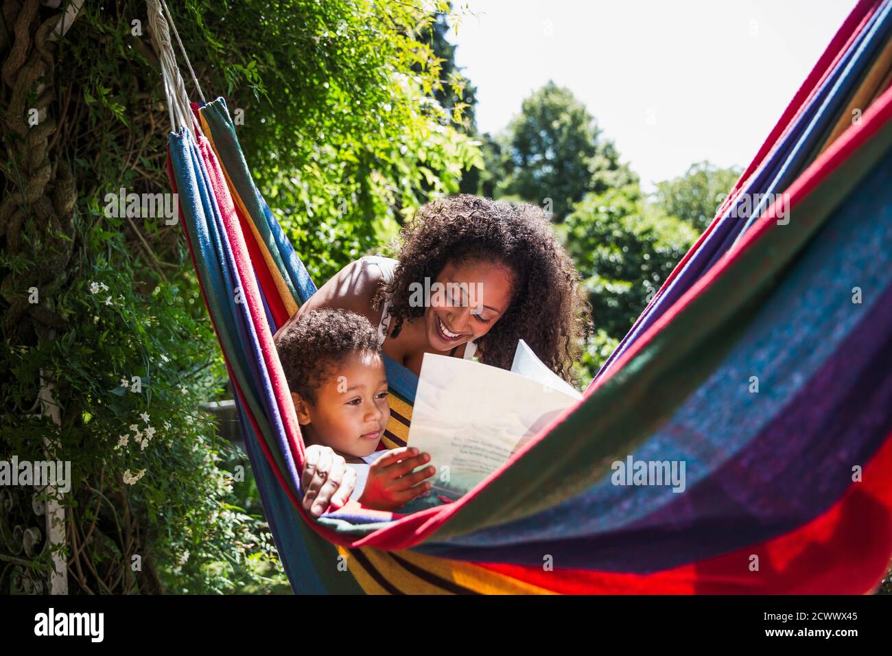 Mother and son reading book in sunny summer hammock in backyard Stock Photo