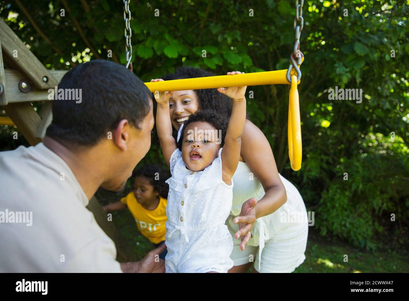 Parents watching happy toddler daughter hanging from swing Stock Photo