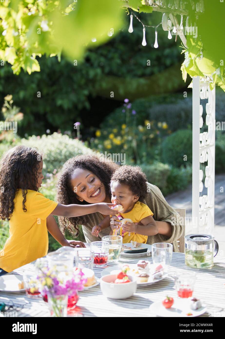 Happy mother and daughters eating at sunny summer garden table Stock Photo
