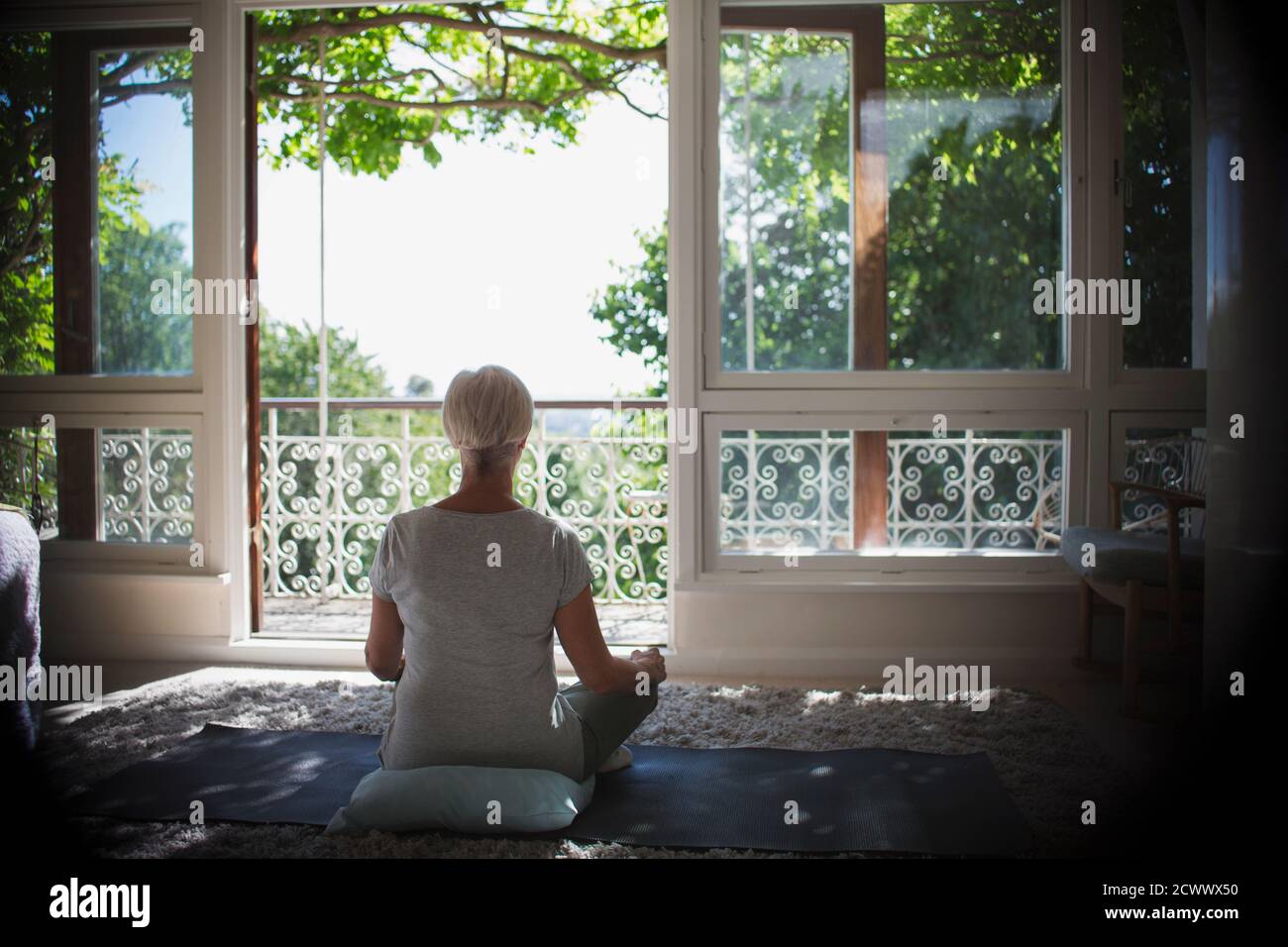 Serene woman meditating at tranquil sunny balcony window Stock Photo
