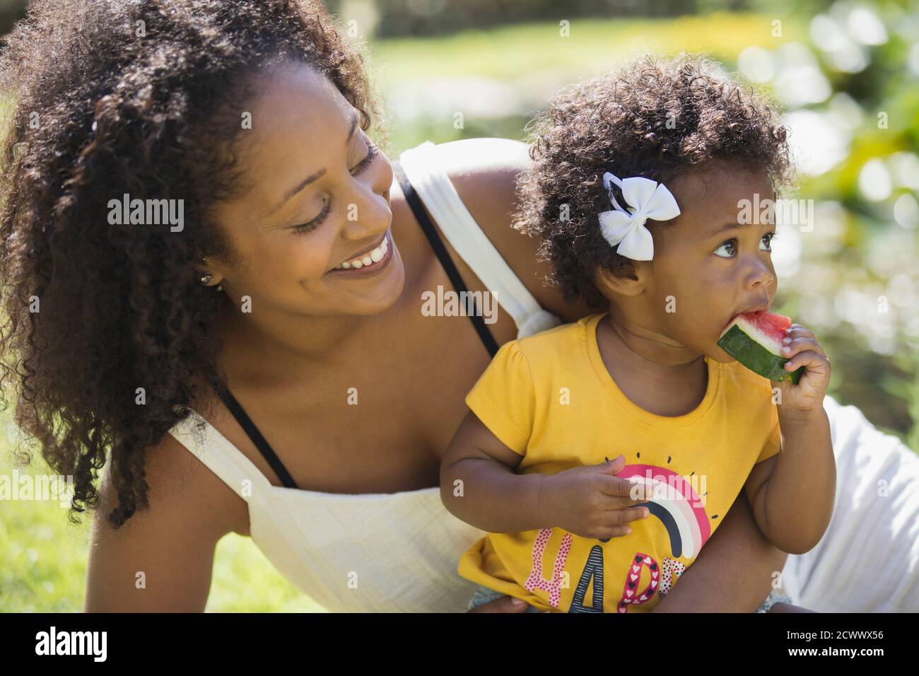 Happy mother watching toddler daughter eating watermelon Stock Photo
