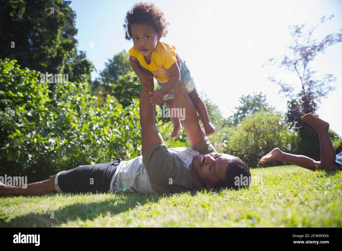 Father lifting cute toddler daughter overhead in sunny summer grass Stock Photo