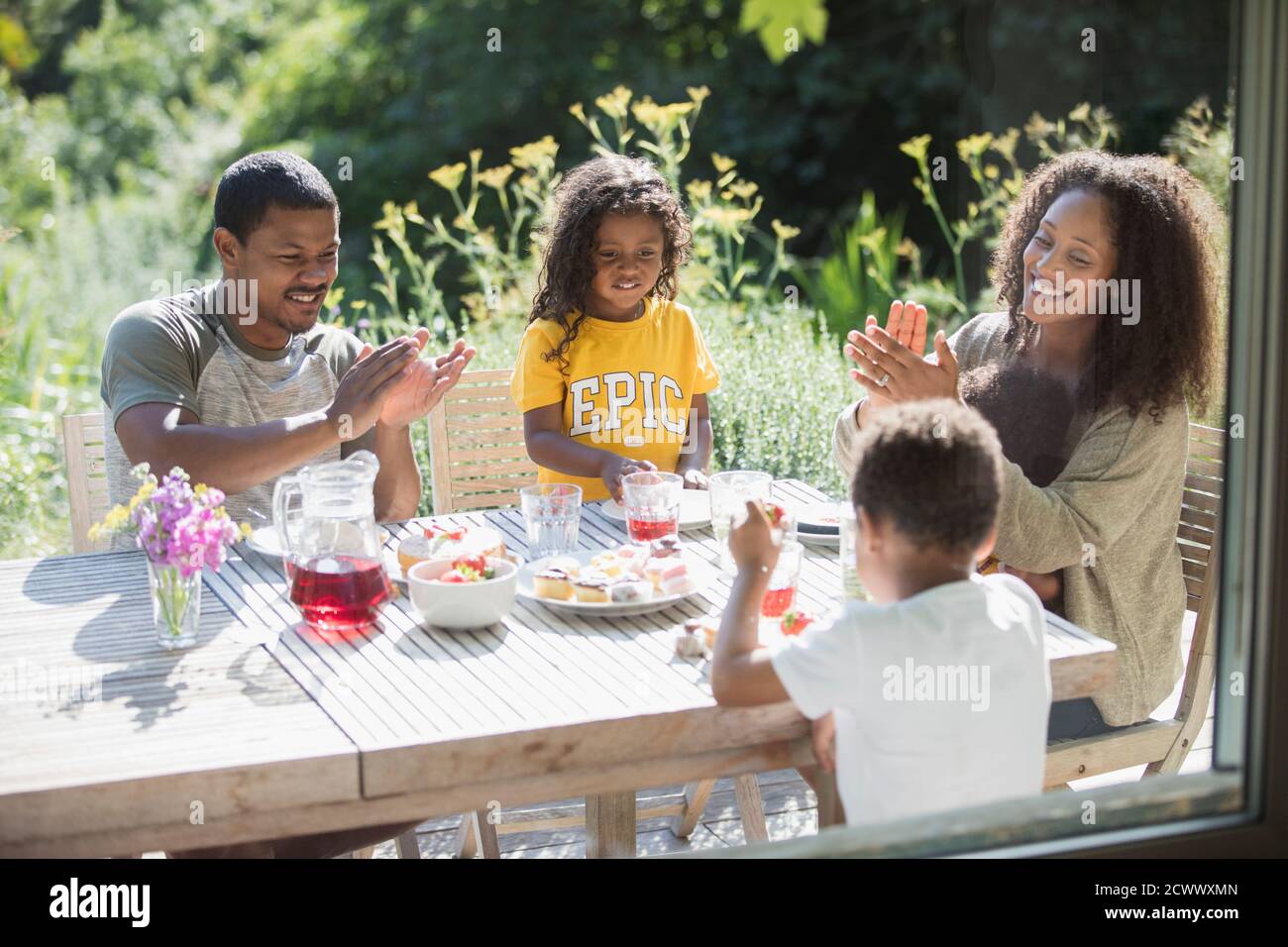 Happy family clapping and eating at sunny summer patio table Stock Photo
