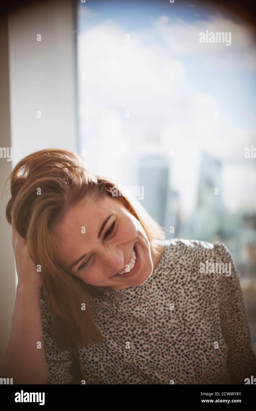 Happy businesswoman laughing with hand in hair at window Stock Photo