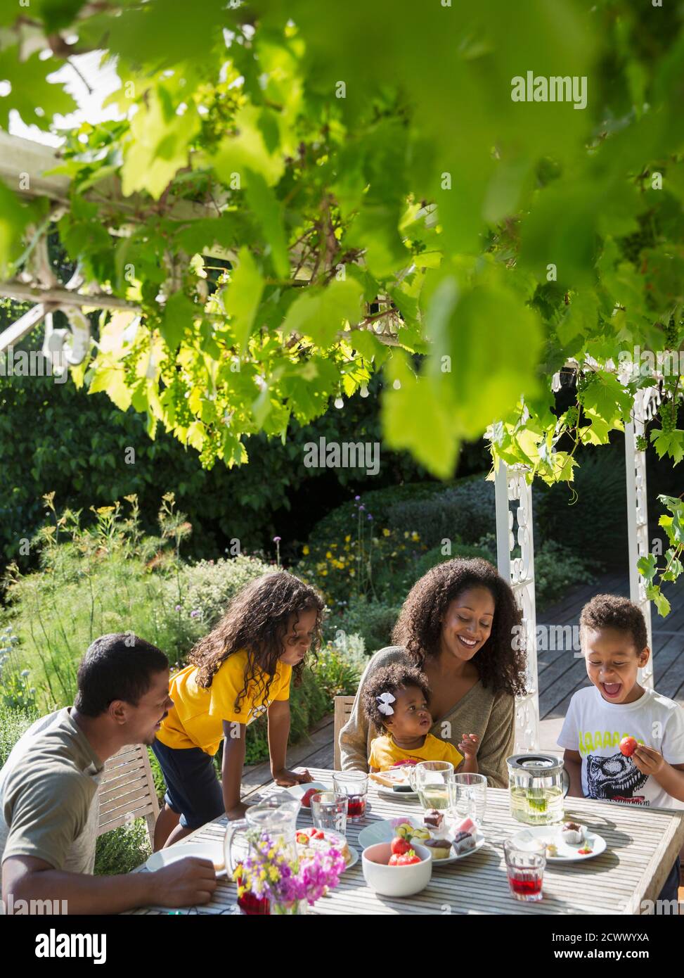 Happy family enjoying lunch at sunny summer garden table Stock Photo
