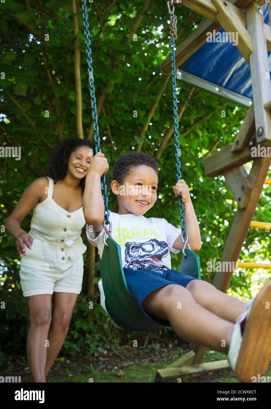 Mother pushing son on swing set in summer backyard Stock Photo