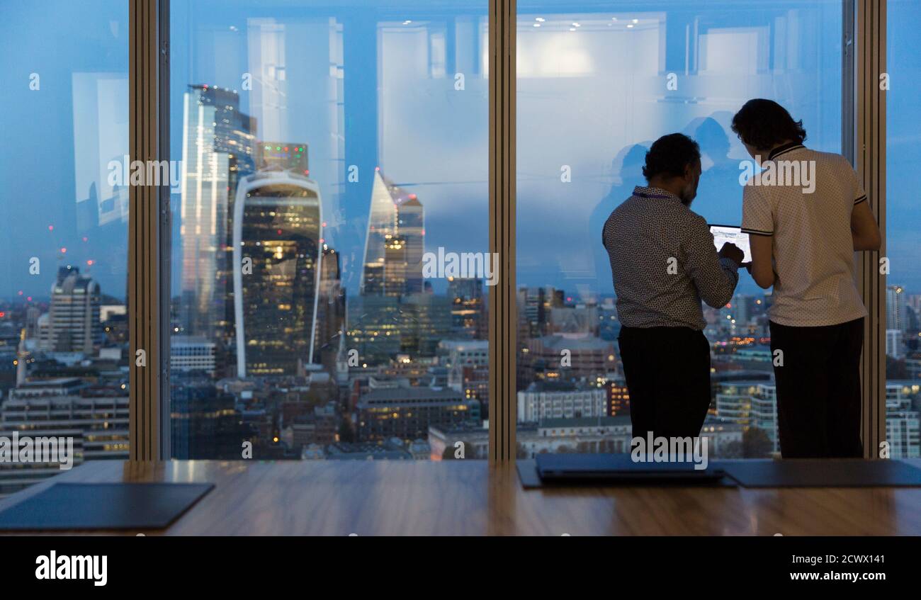 Businessmen working late at highrise office window, London, UK Stock Photo