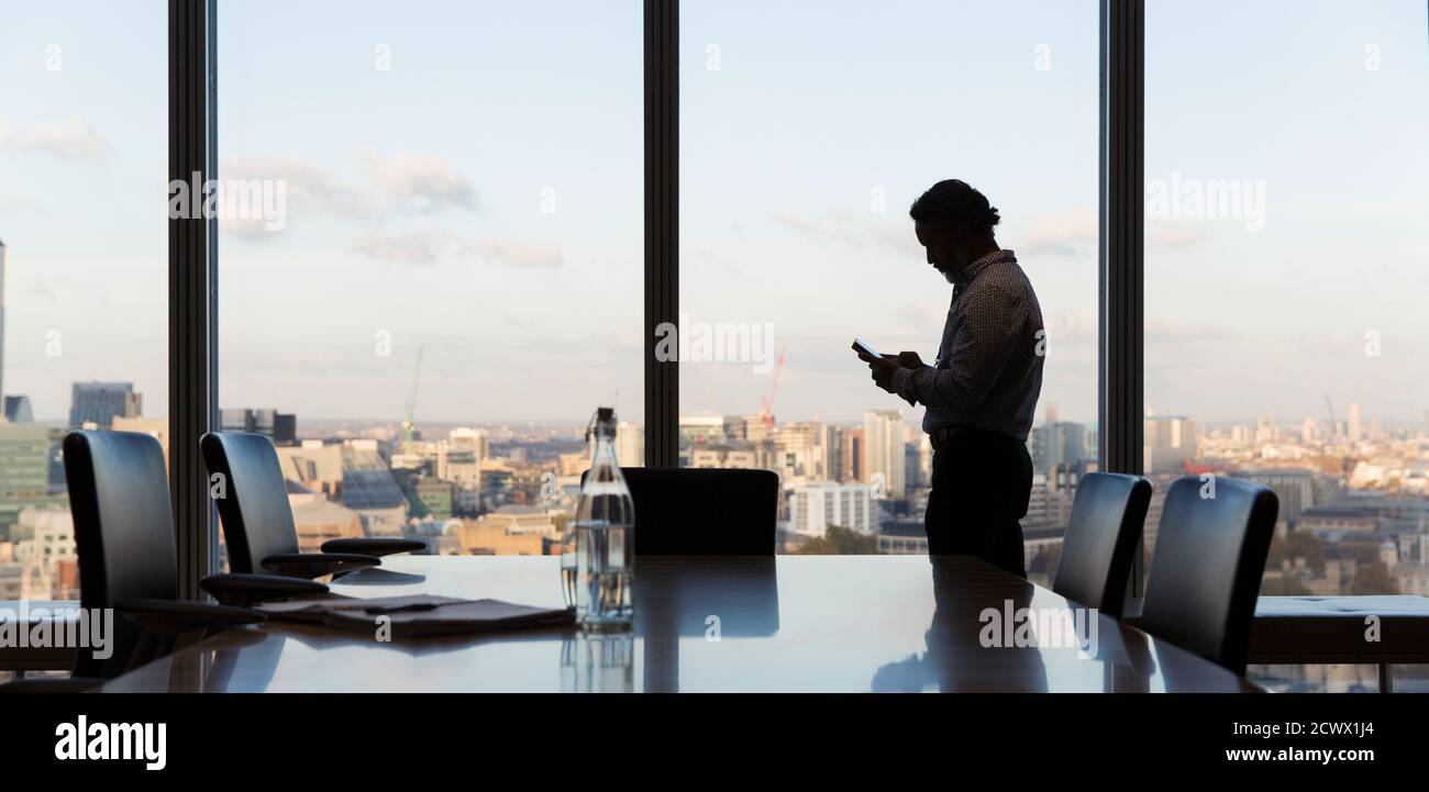 Businessman using smart phone at highrise office window, London, UK Stock Photo