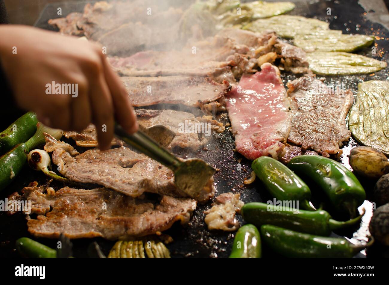 Closeup of a person roasting meat with welsh onions, jalapenos, and