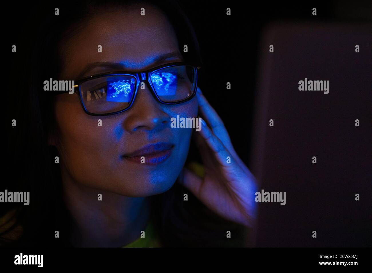 Close up laptop reflection in eyeglasses of businesswoman working late Stock Photo