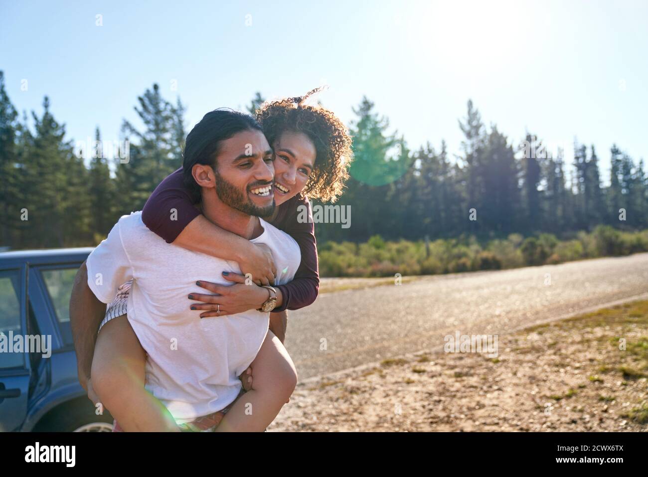 Happy affectionate couple piggybacking at sunny summer roadside Stock Photo