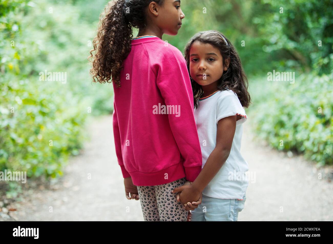 Portrait affectionate sisters holding hands on park path Stock Photo