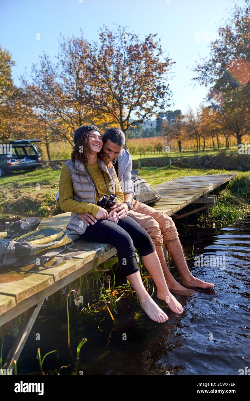 Affectionate barefoot young couple laughing on sunny dock Stock Photo