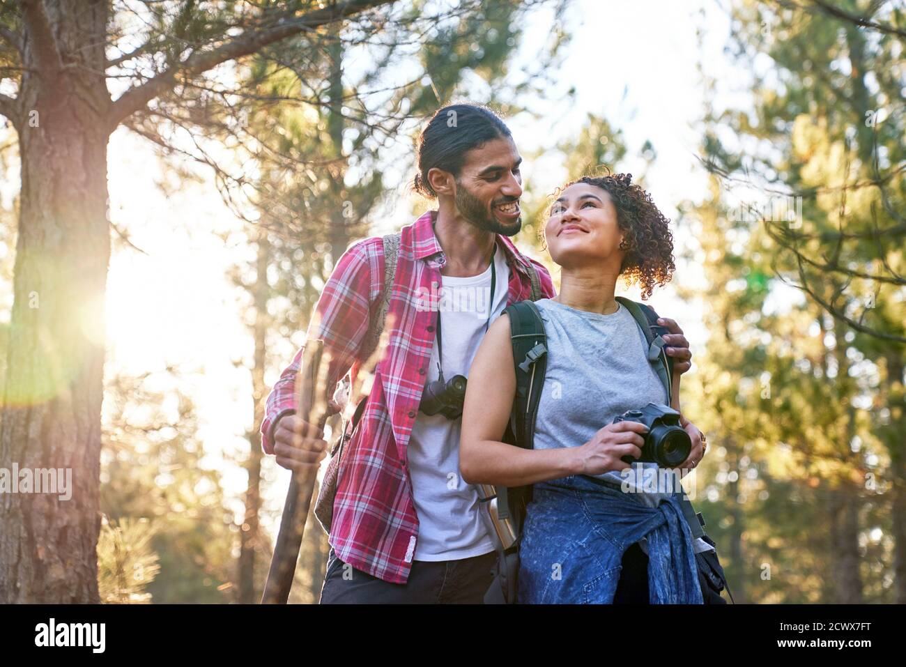 Happy affectionate young couple hiking with camera in sunny woods Stock Photo