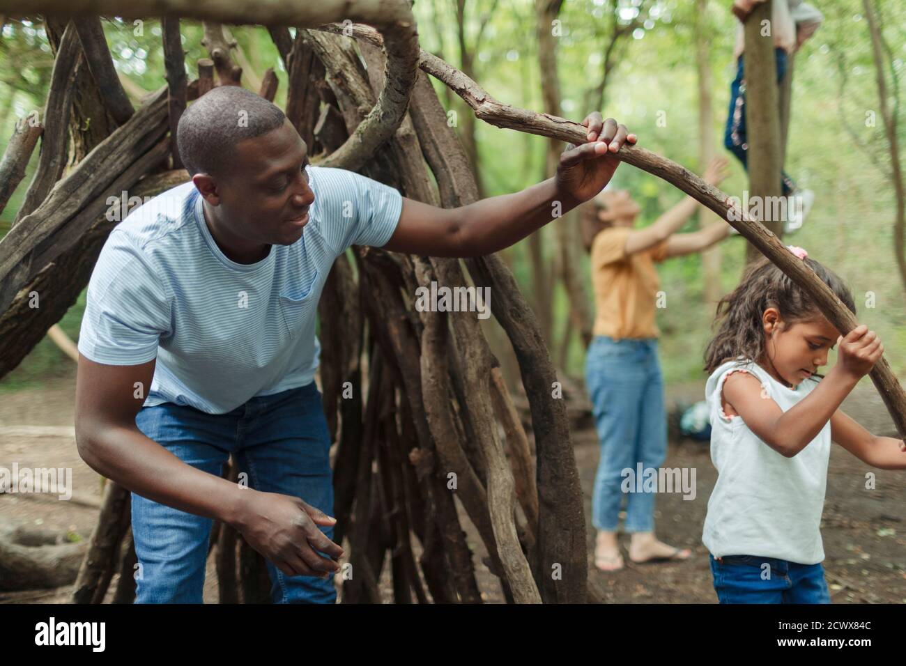 Father and daughter building fort with tree branches in woods Stock Photo