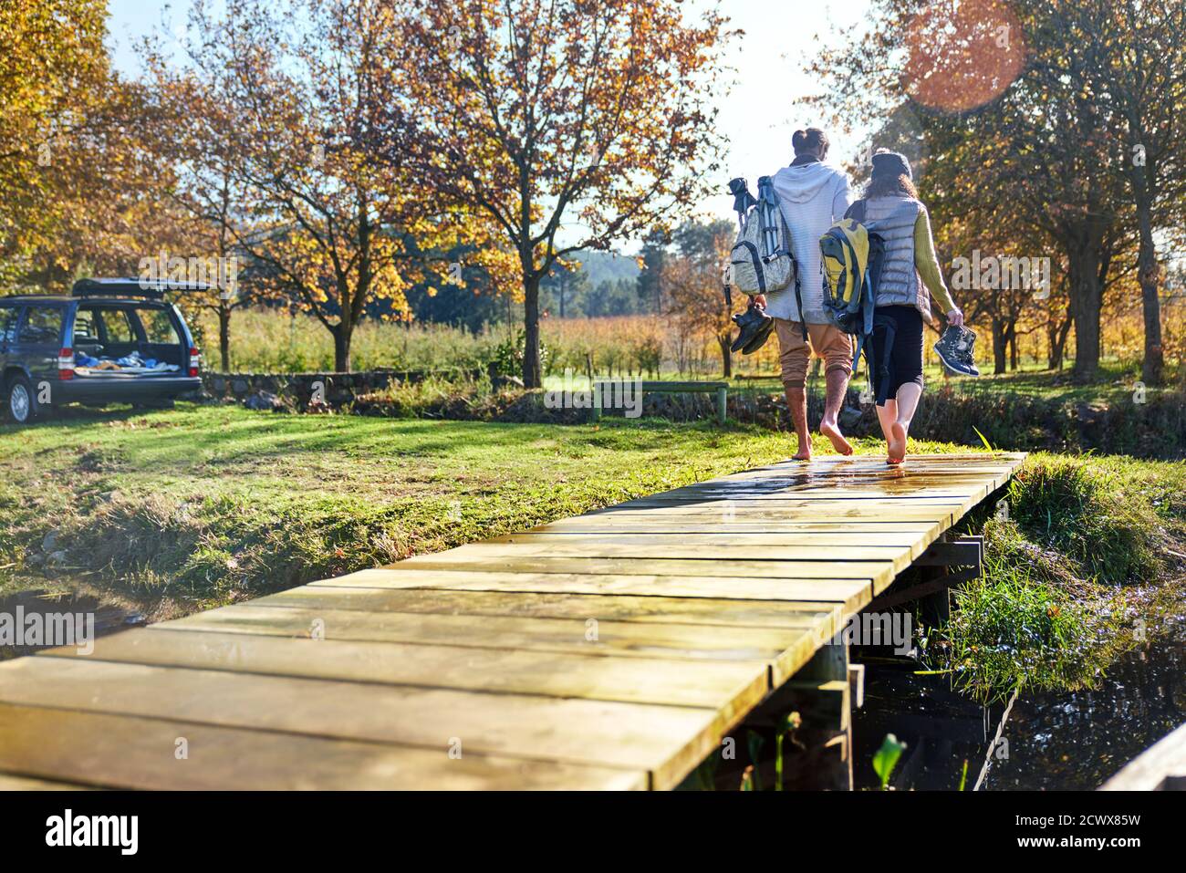 Barefoot young couple walking on sunny autumn lakeside dock Stock Photo