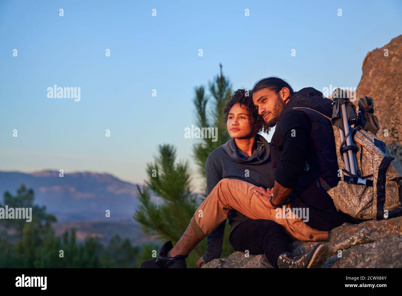 Serene young hiking couple enjoying sunset on rocks Stock Photo